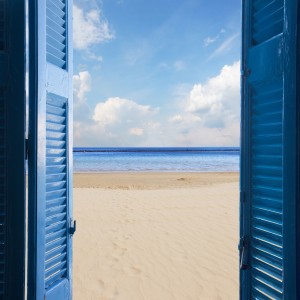 new beginings concept - open blue door to sandy beach and sky with sunshine